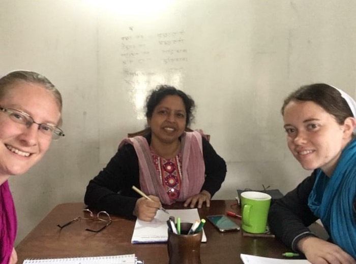 BLCC students practicing Bangla script with their teacher at a classroom table